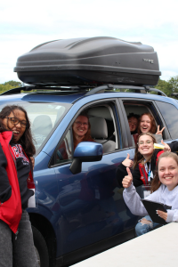Student checking into residence in blue car with other students smiling and giving a thumbs up