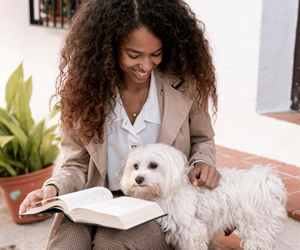 A female student reading a book outdoors with her service dog by her side