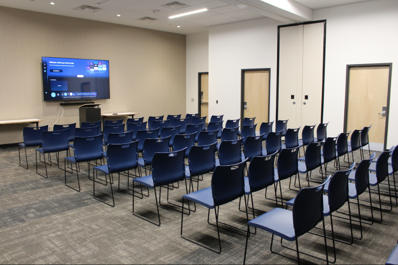 Theater space located on the main floor of Rideau House. There are plenty of blue chairs and a large TV located at the front of the room.