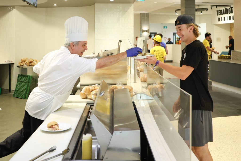 A chef handing a plate of food to a Carleton student in the Teraanga Commons Dining Hall.