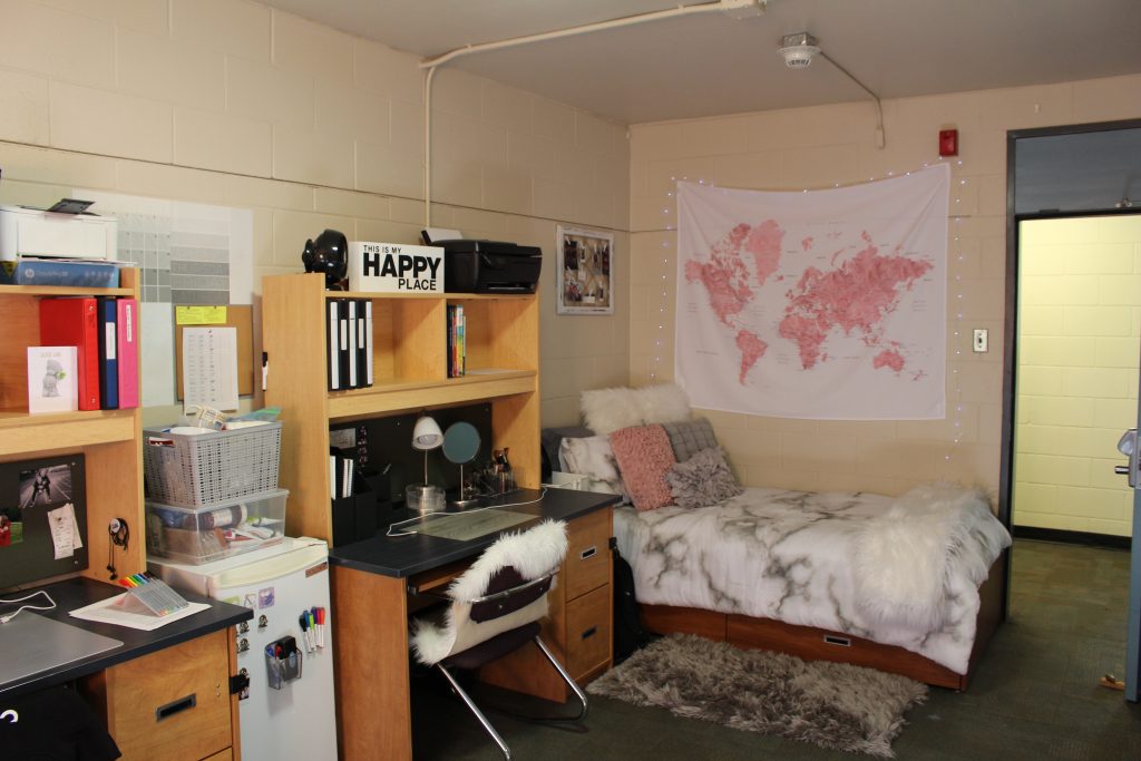 A decorated residence room with a bed, desks and a map