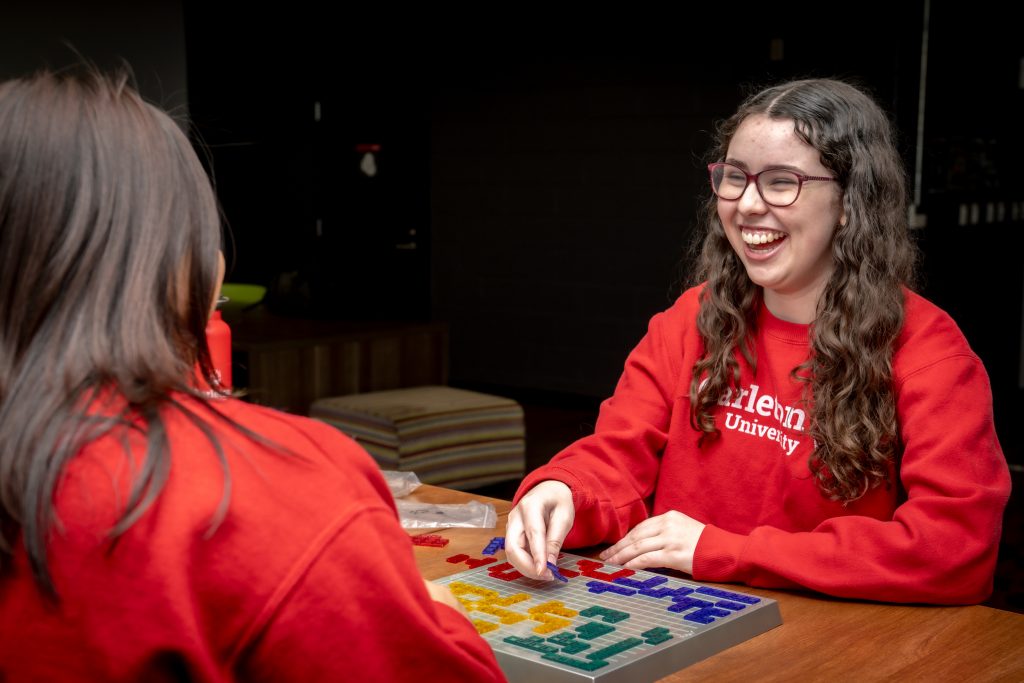 Two students from Carleton are playing a board game together, laughing and enjoying themselves.