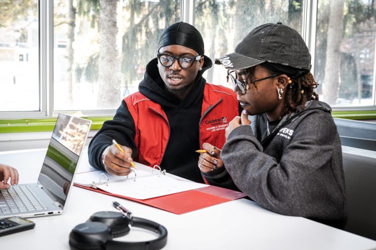 Two Carleton students engaged in a discussion in the study lounge, with big windows in the back.