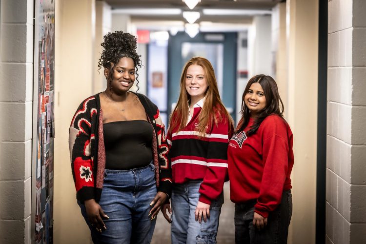 Three Carleton students, smiling and standing in a residence hallway