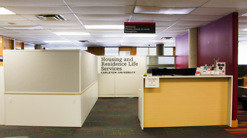 The front reception of the Housing and Residence Life Services, with its sign in the center of the image and the main desk to its right