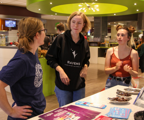 Three students talk over a display at the caf