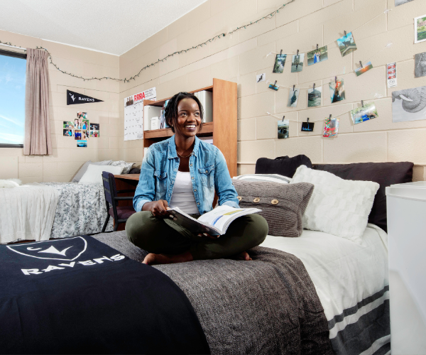 A student sits cross legged on her bed in residence