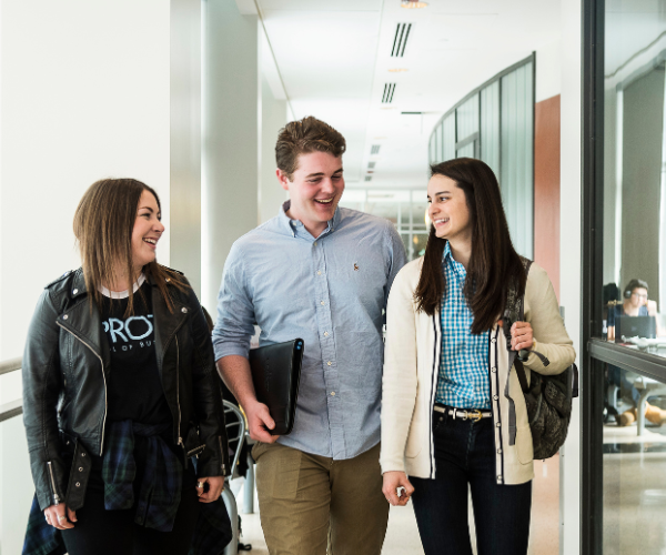 Three students walk down a hall while talking